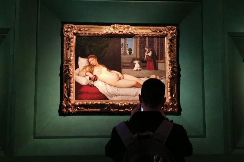 Persona fotografiando obras de arte enmarcadas en una galería.