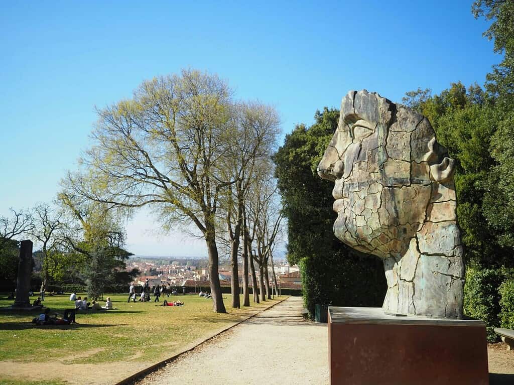 Large cracked face sculpture in outdoor park setting.